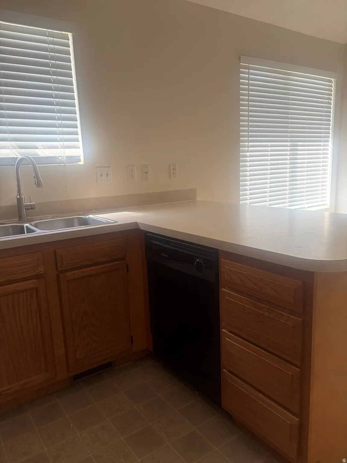 Kitchen featuring a double basin sink, dark finish dishwasher, wood-finish cabinetry, and solid surface countertops