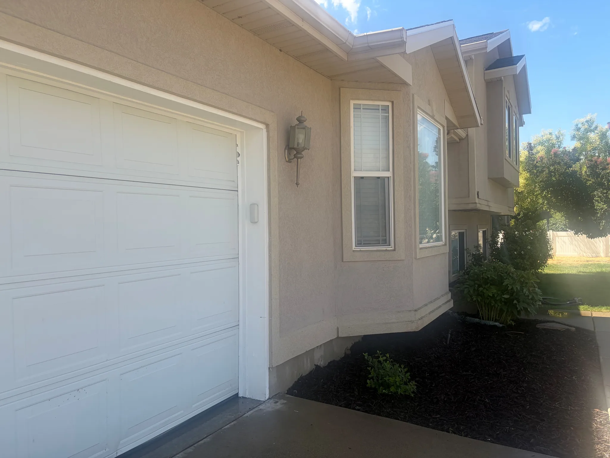 Stucco exterior with a paneled garage door, decorative exterior light fixture, bay windows, and dark ground cover