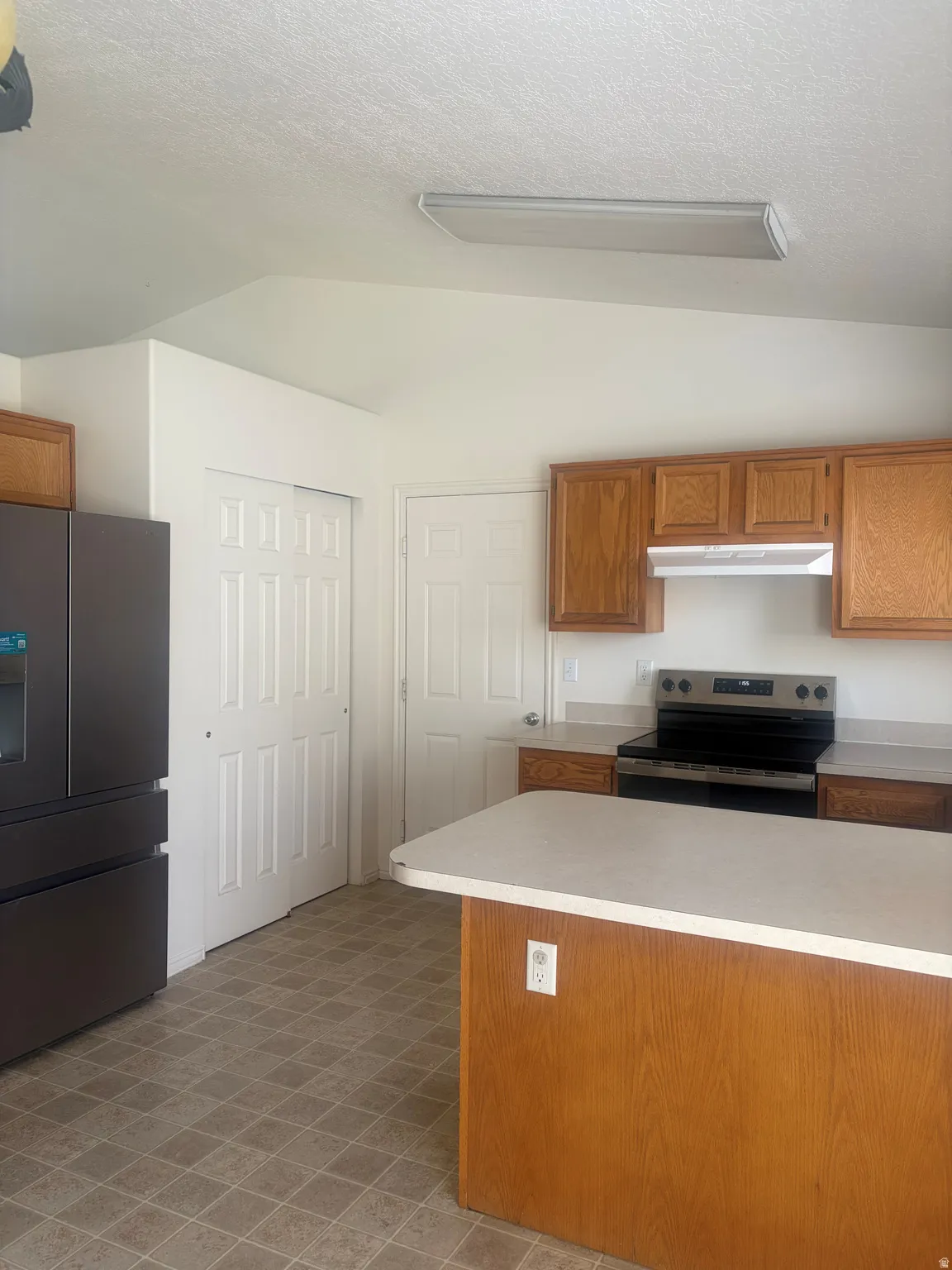 Kitchen featuring wood-finish cabinetry, a central island with a light-colored countertop, and a built-in range with an overhead microwave