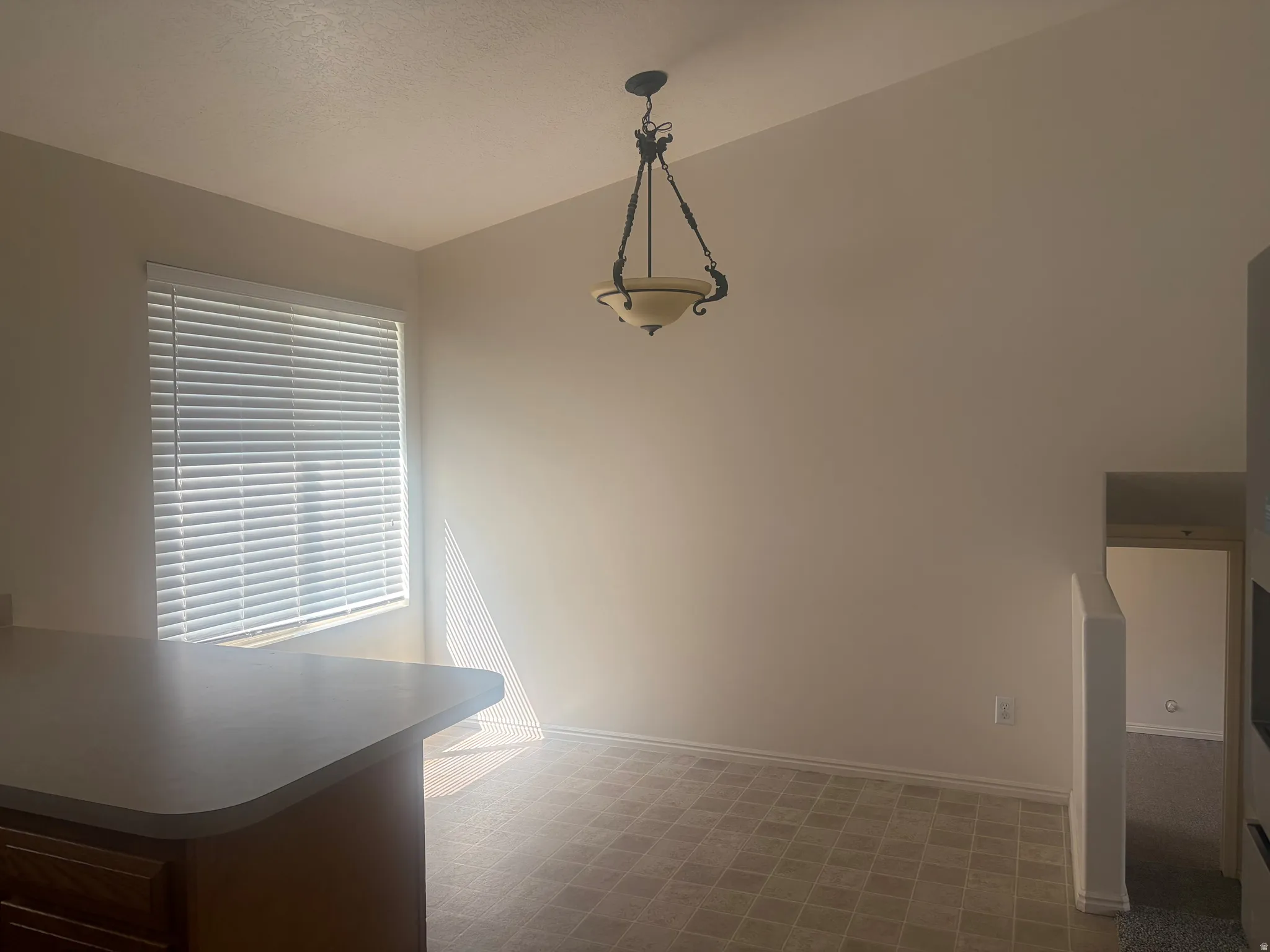 Vaulted ceiling with an attached pendant light fixture, window with blinds, and tile flooring