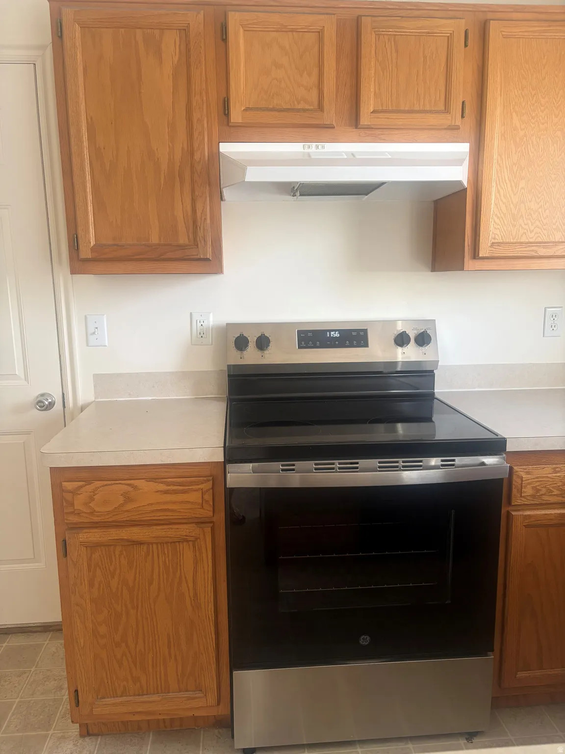 Kitchen featuring wood cabinetry, light-toned countertops, a stainless steel electric range, and a white range hood