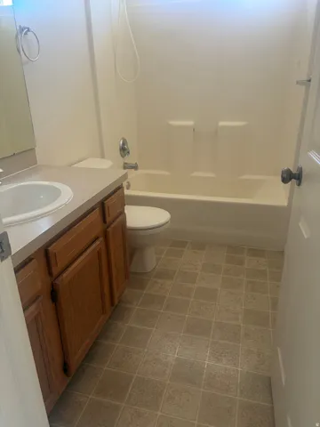 Bathroom featuring a built-in vanity with wood-finish cabinetry, a white drop-in sink, and a combination tub/shower