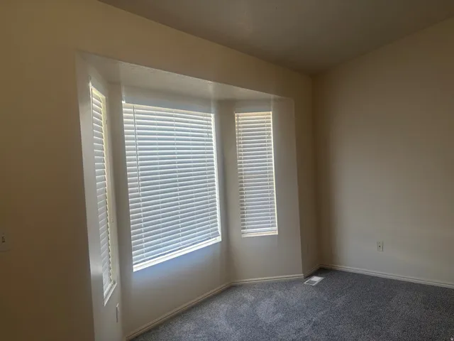 Bay window with white blinds, neutral wall color, and plush gray carpeting
