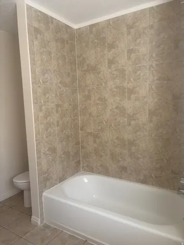 White bathtub with chrome fixtures, surrounded by neutral-toned wall tiles extending to the ceiling