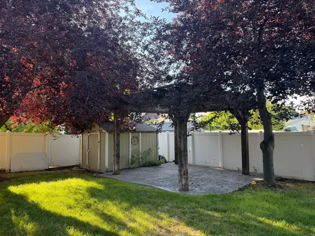 Back yard- Lush landscaping with mature trees, a wood pergola, a concrete patio, a storage shed, and white privacy fencing