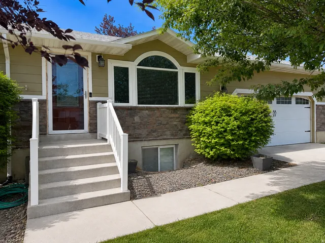 Expansive front facade featuring a stone accent wall, arched window, attached garage, and concrete steps with white railings