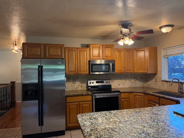 Kitchen featuring wood cabinetry, stainless steel appliances, speckled countertops, and a ceiling fan with integrated lighting