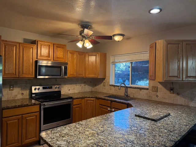 Wood cabinetry with stainless steel appliances, granite-patterned countertops, and a tiled backsplash