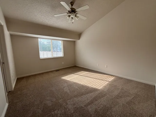 Room with sloped ceiling, light tan carpeting, and a ceiling fan with light fixture