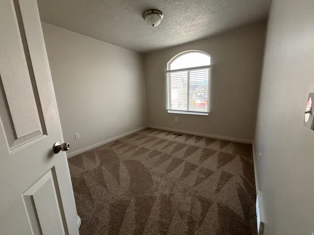 Arched window with blinds, vaulted ceiling, neutral wall paint, patterned carpeting, and a flush mount light fixture
