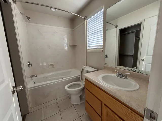 Bathroom featuring a built-in bathtub, shower with white surround, single vanity with wood-finish cabinetry, and tiled flooring