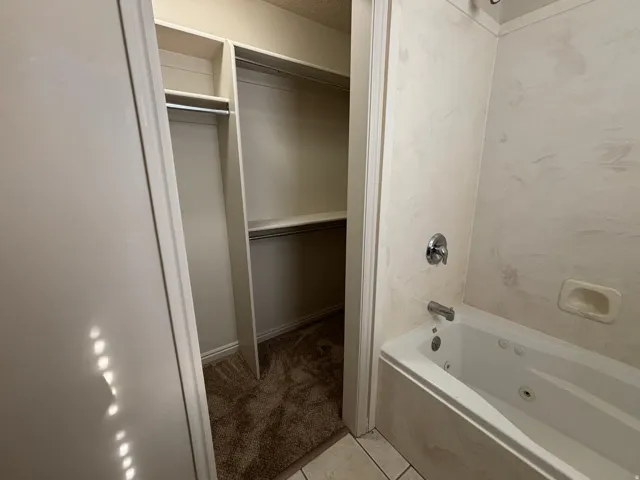 Built-in closet shelving, integrated hanging rods, wall-mounted bathtub fixtures, and a white soaking tub with jets