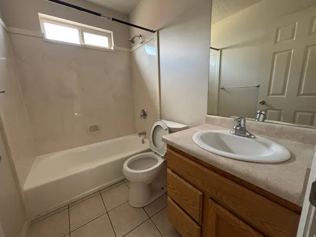 Bathtub with a shower fixture, a toilet, a vanity with an integrated sink, a large wall-mounted mirror, and tile flooring
