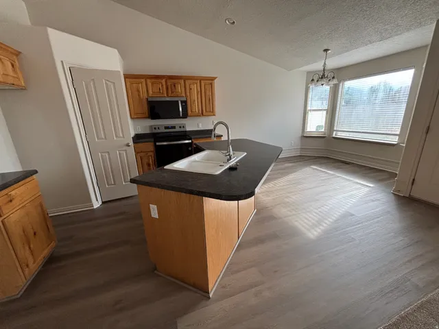 Kitchen featuring wood cabinetry, dark countertops, a built-in microwave, and a stainless steel sink