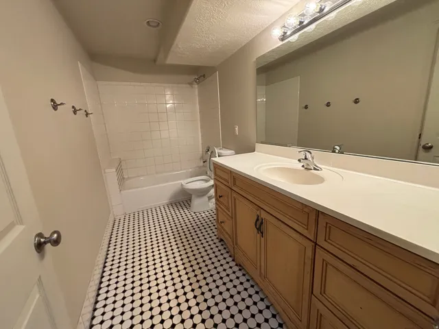 Bathroom featuring a full vanity with an integrated sink, a large wall-mounted mirror, a tub and shower combination with white tile surround, and black and white penny tile flooring