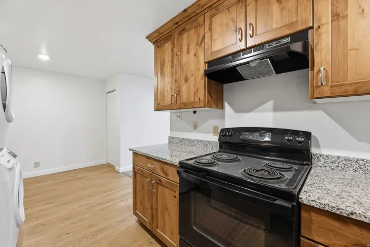 Wood-finish flooring, ample wood cabinetry, black range and oven, stone-finish countertops, and recessed lighting