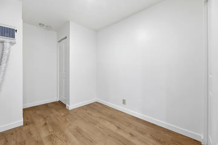 Wood-finish flooring with white baseboards, white walls, and a white paneled door