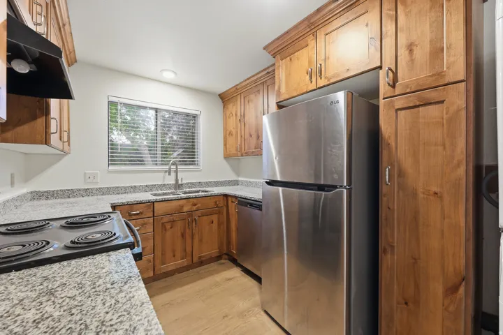 Kitchen featuring wood cabinetry, stainless steel appliances, speckled countertops, and wood-finish flooring