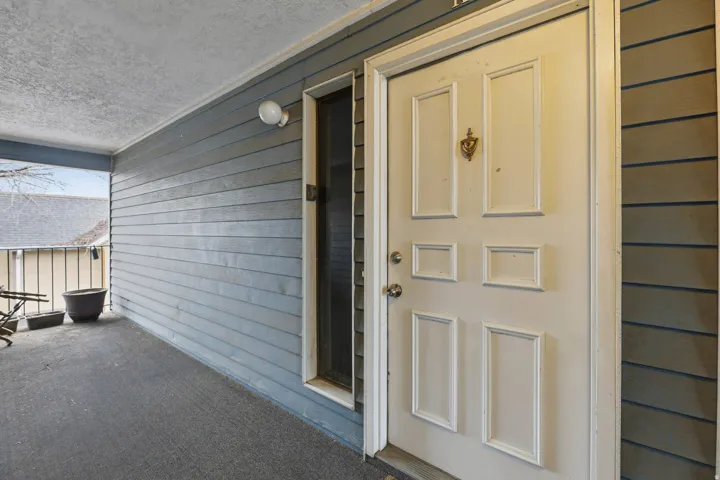 Covered porch with a white panel door, horizontal siding, and a built-in light fixture