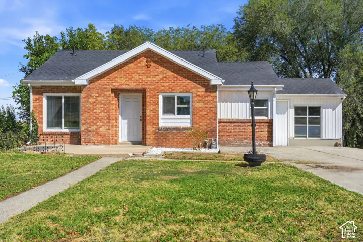 Brick and vertical siding exterior with a dark shingle roof, concrete walkway, and a paved driveway