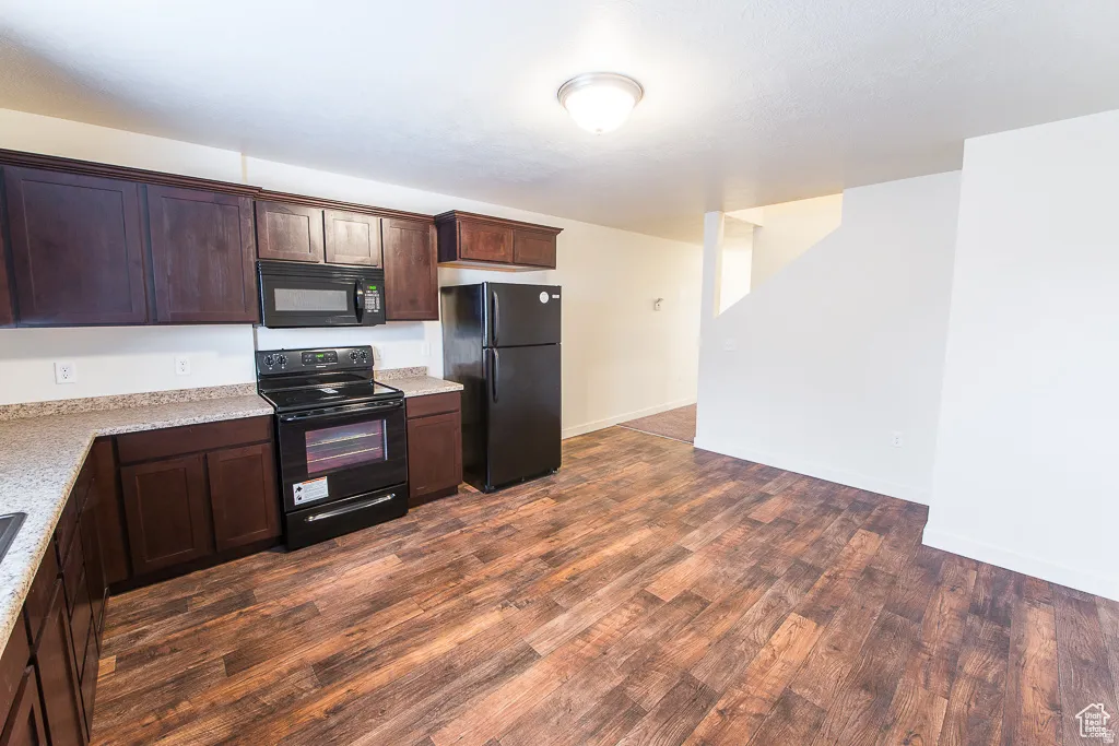 Kitchen featuring dark wood-finish cabinetry, black appliances, light-toned countertops, and wood-finish flooring