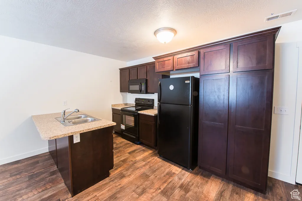 Kitchen featuring wood-finish flooring, dark wood cabinetry, light-toned countertops, and black appliances