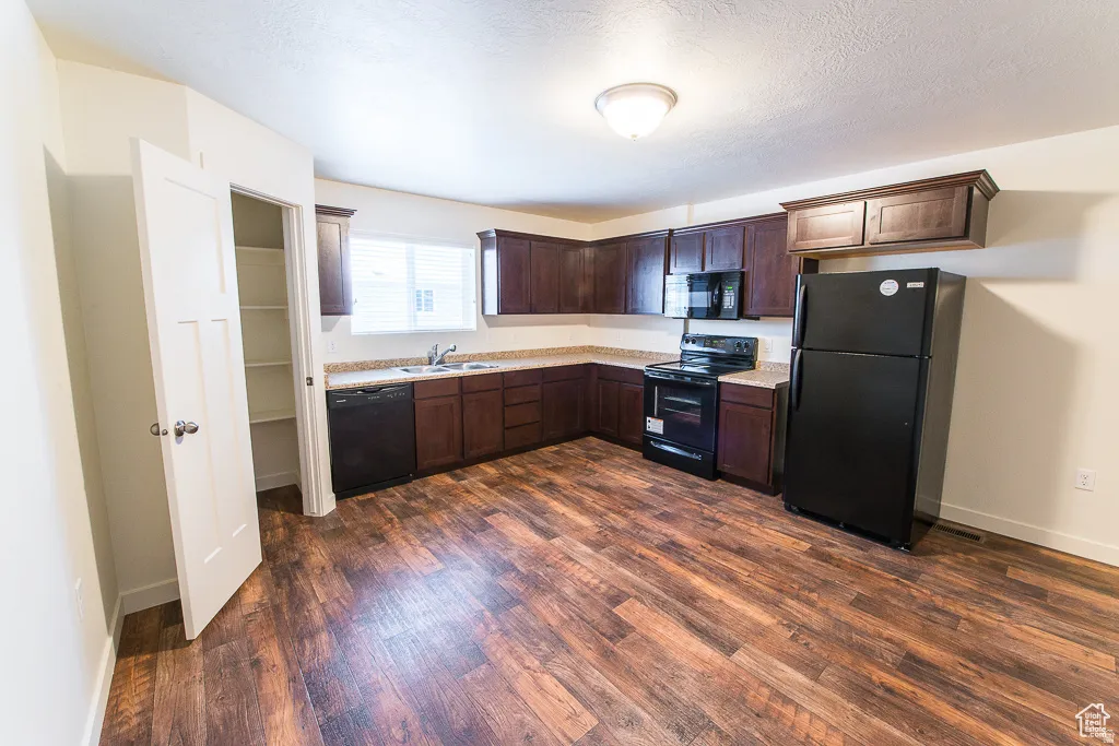 Kitchen featuring wood-finish flooring, dark wood-finish cabinetry, built-in black appliances, and a pantry with shelving