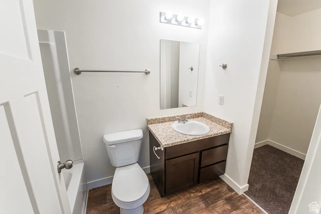 Vanity with granite-style countertop, integrated sink, wood-finish flooring, and wall-mounted lighting fixture