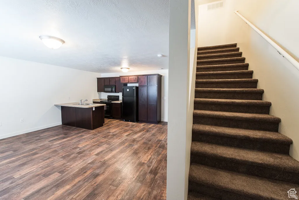 Kitchen with dark wood-finish cabinetry, black appliances, and a breakfast bar with a sink