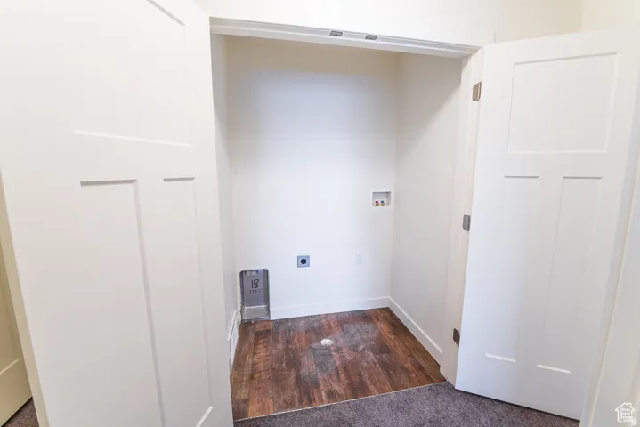 Utility closet featuring wood-finish flooring, white paneled doors, and built-in laundry hookups