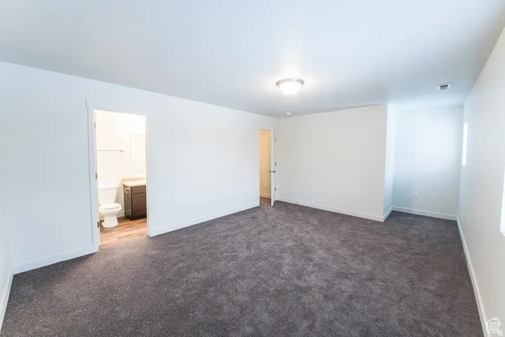 Spacious room with dark gray carpeting, crisp white walls, and a ceiling-mounted light fixture
