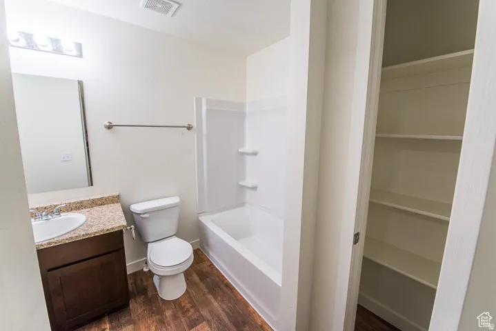 Wood-finish flooring, built-in storage shelving, a shower and tub combination, a vanity with a counter and integrated sink, and a mirrored medicine cabinet