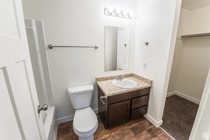 Vanity with granite-style countertop, integrated sink, wood-finish flooring, and wall-mounted lighting fixture