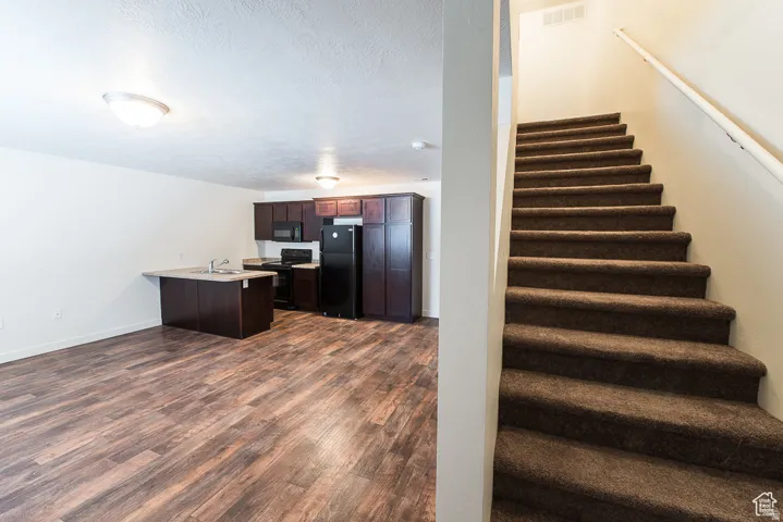 Kitchen with dark wood-finish cabinetry, black appliances, and a breakfast bar with a sink