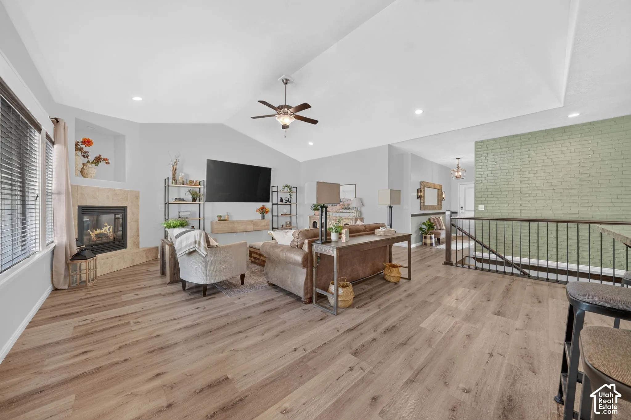 Vaulted ceiling featuring a ceiling fan, wood-finish flooring, a fireplace with a stone surround, and a wrought iron railing