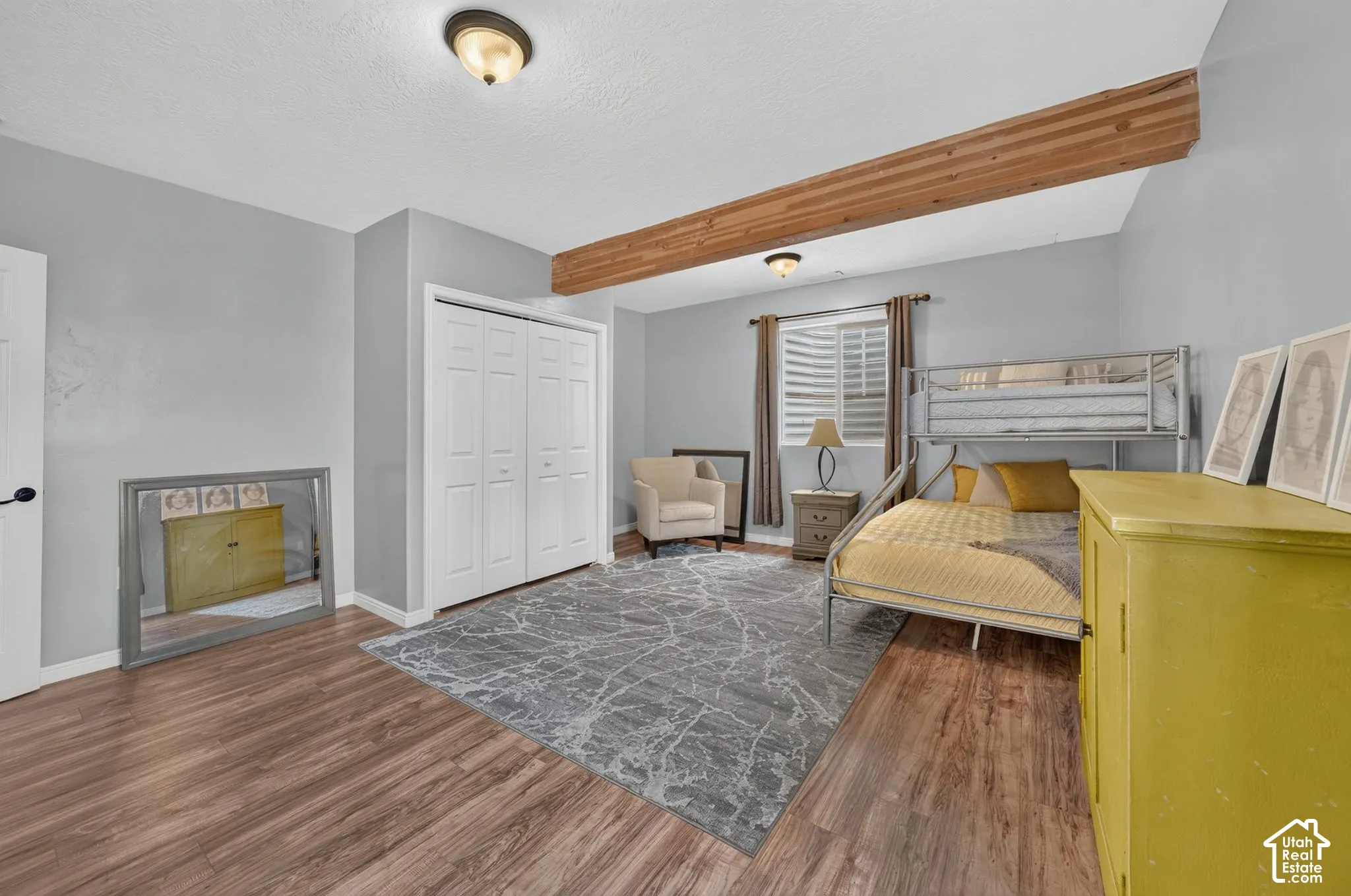 Wood-finish flooring, white bi-fold closet doors, exposed wood beam, recessed window with blinds, and flush-mount lighting