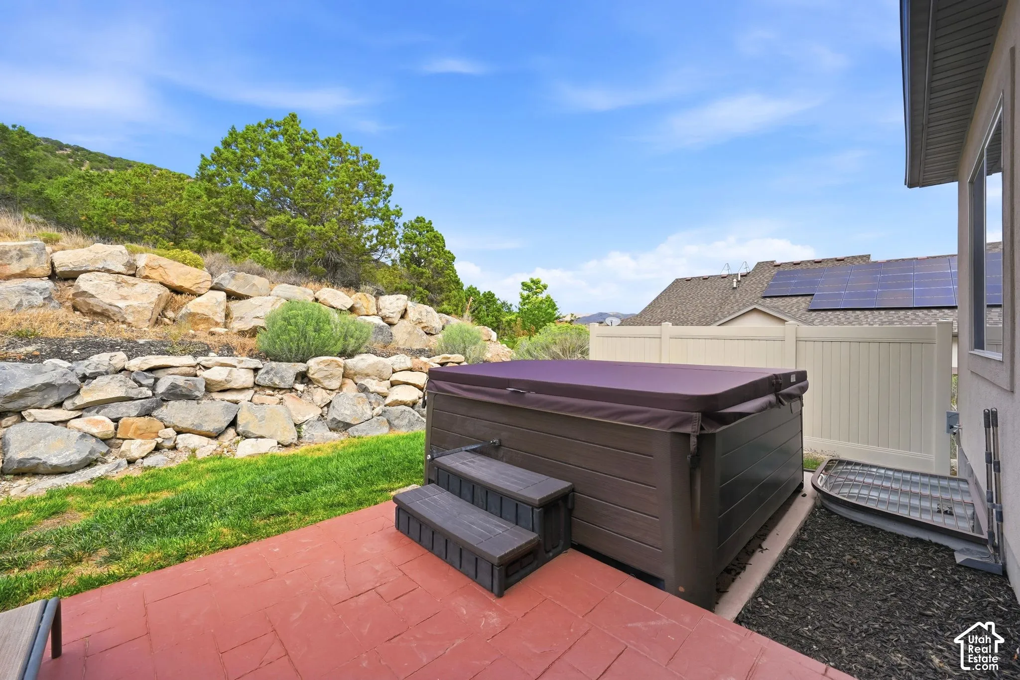 Patio with a hot tub, rock retaining wall, and backyard green space