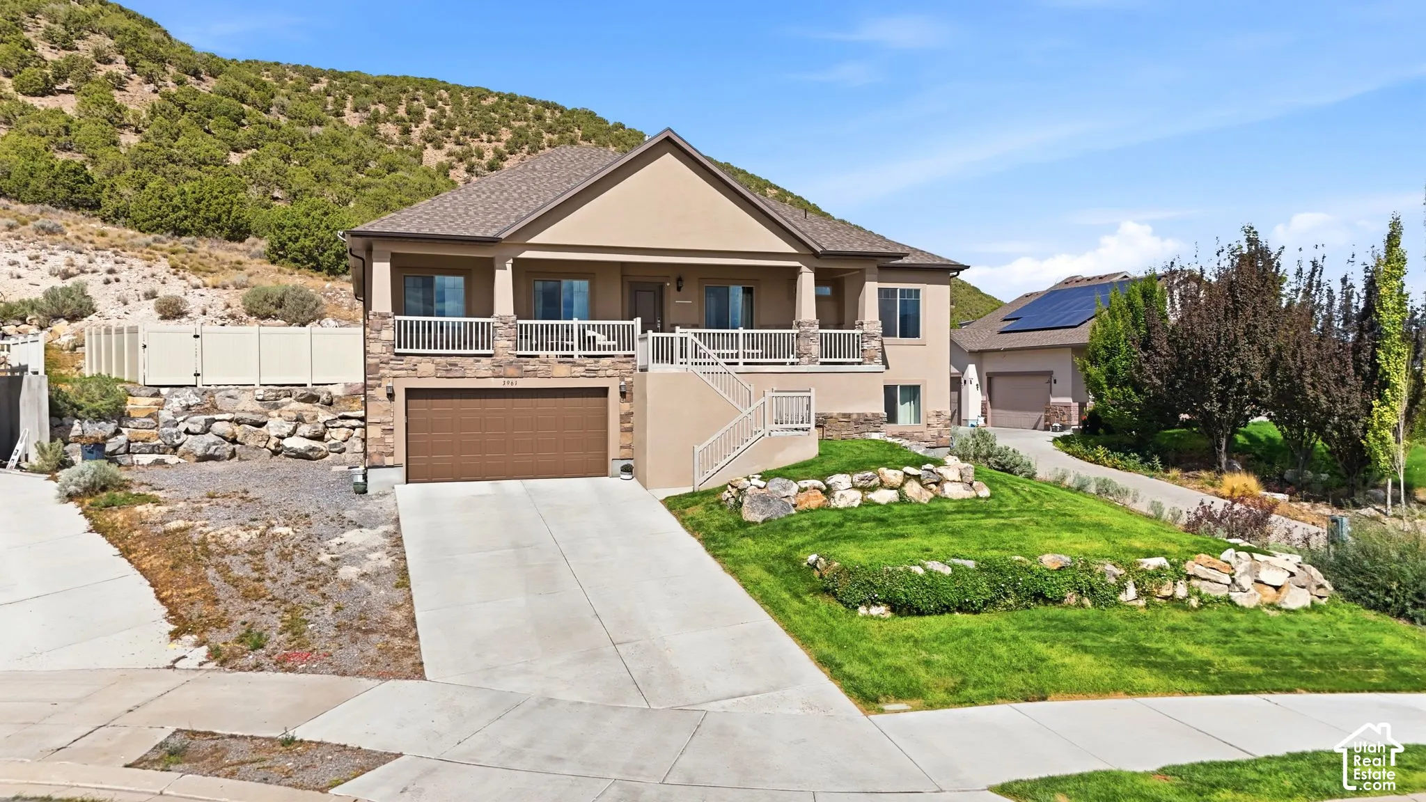 Stucco and stone exterior with a two-car garage, mature landscaping, and a covered balcony