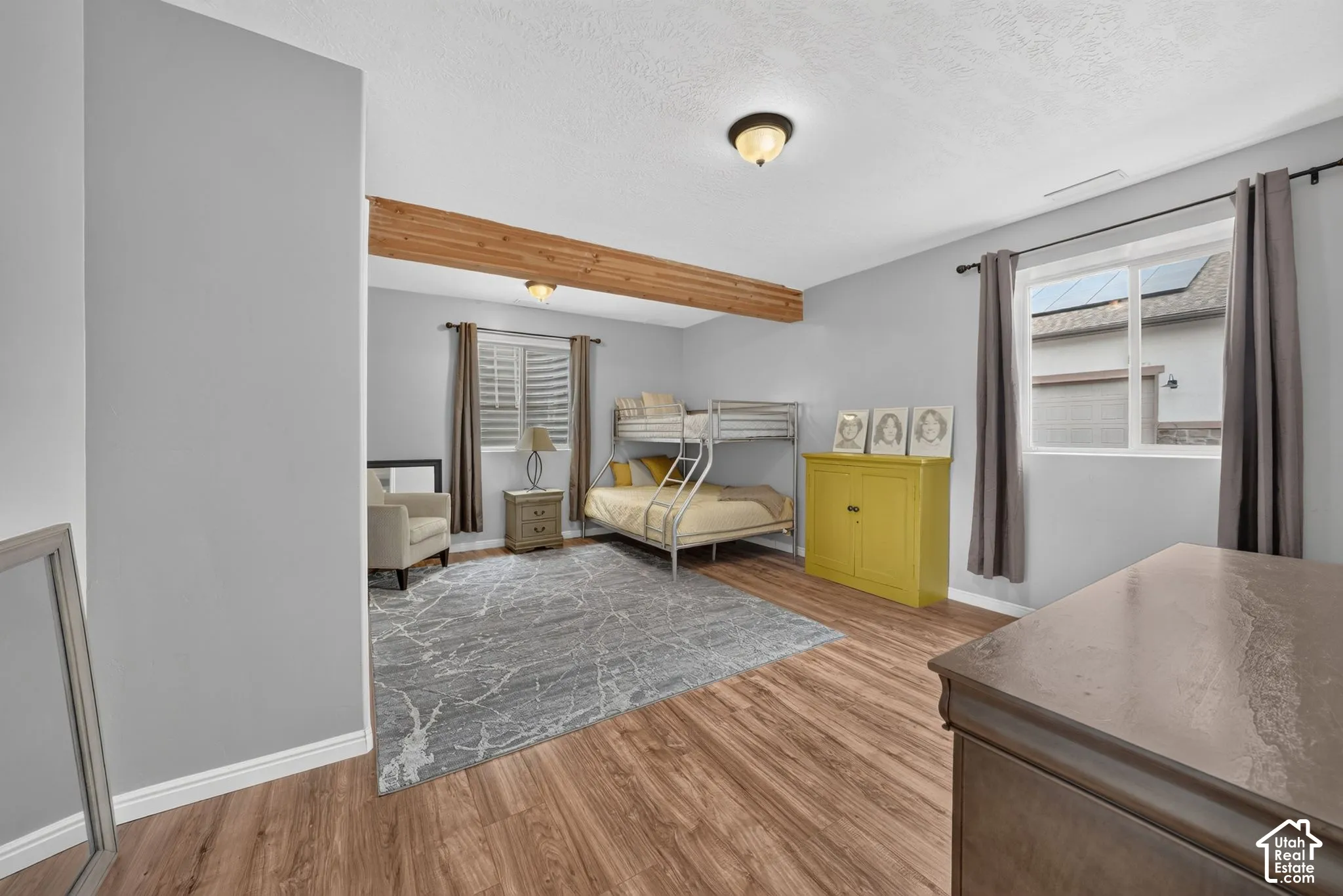 Wood-finish flooring, exposed wood beam, recessed window with blinds, and ceiling-mounted light fixtures