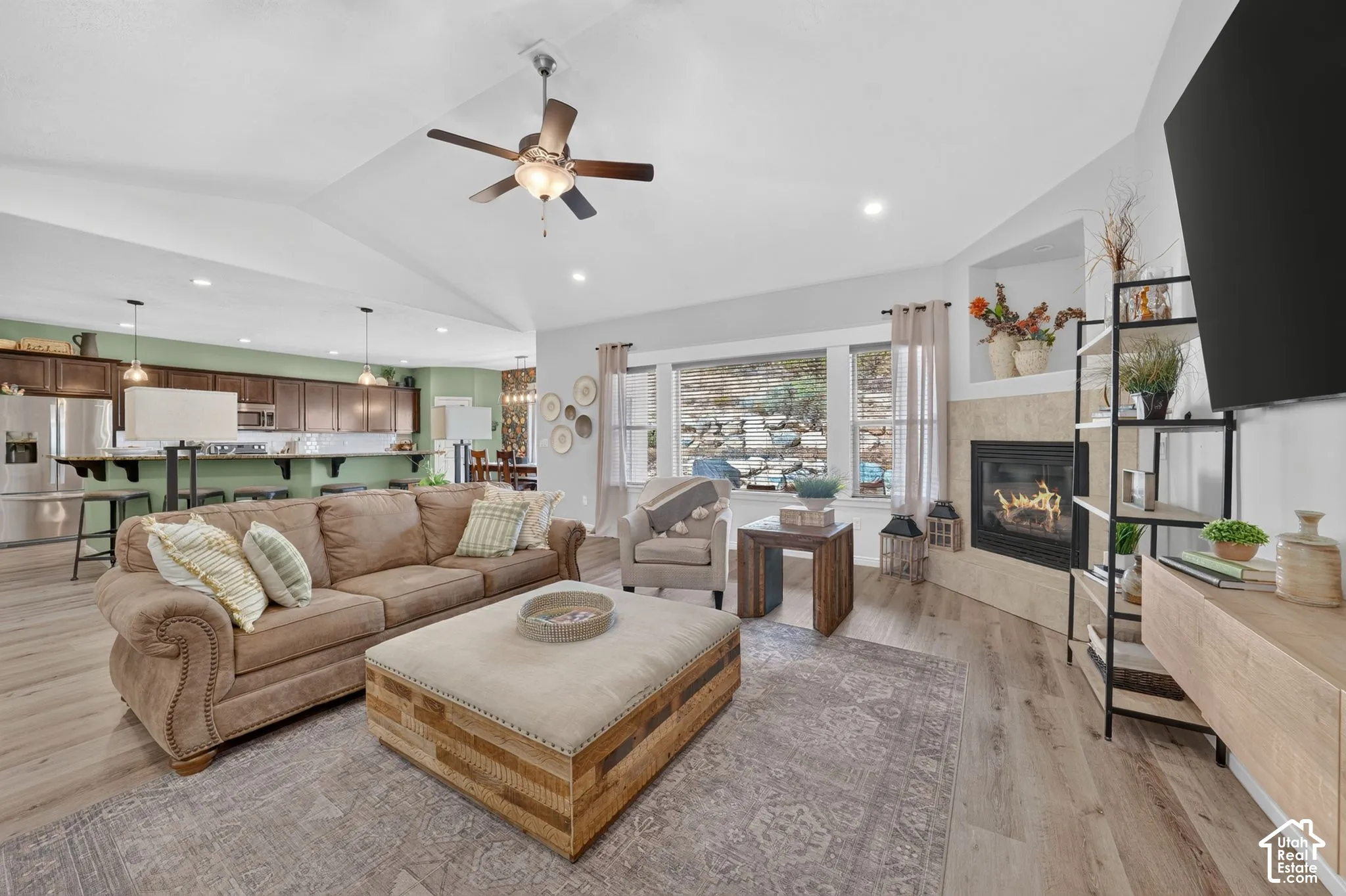 Vaulted ceiling, recessed lighting, wood-finish flooring, corner fireplace with tile surround, and built-in shelving