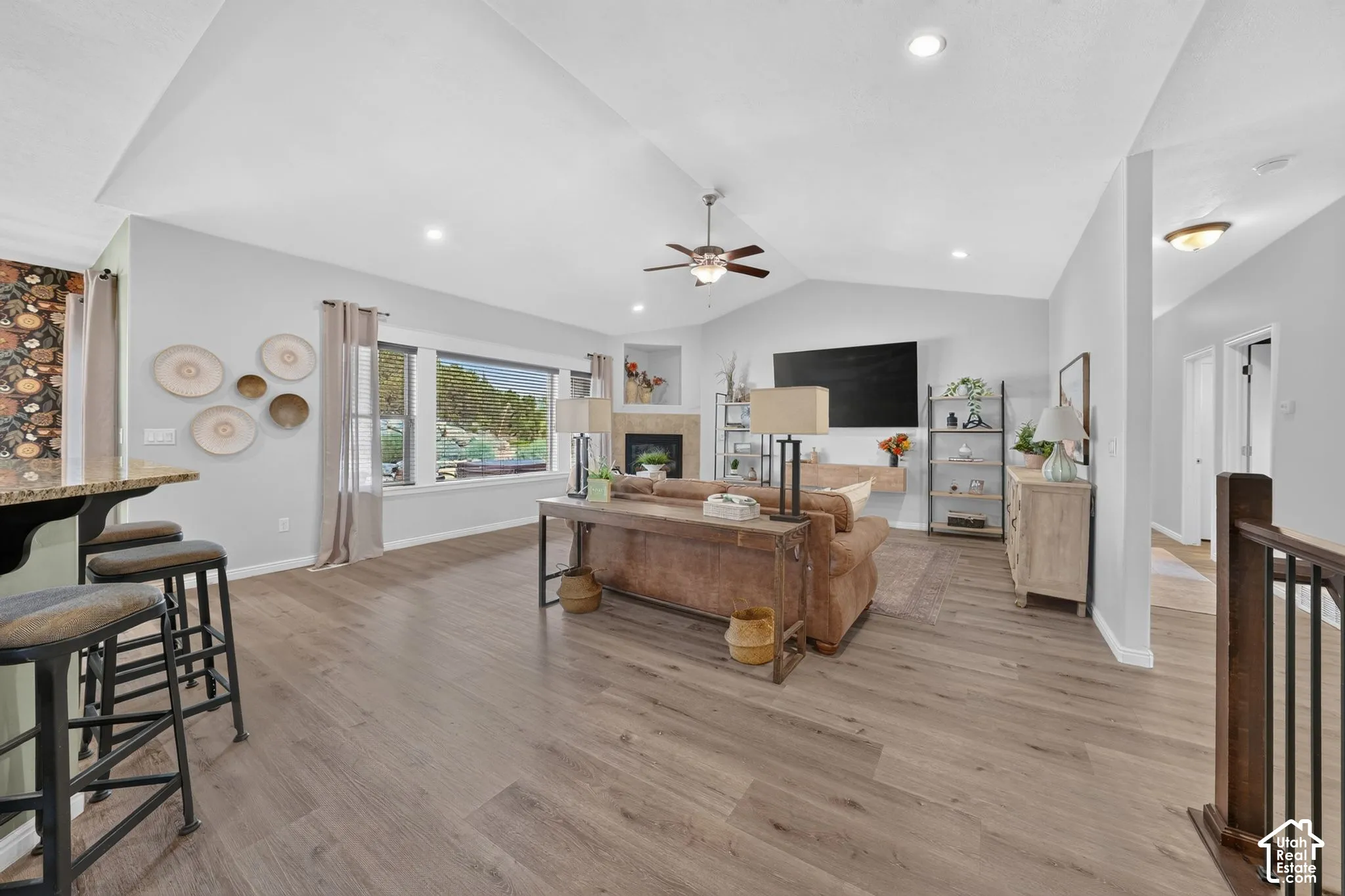 Vaulted ceilings with recessed lighting, wood-finish flooring, a fireplace with a stone surround, and a large picture window