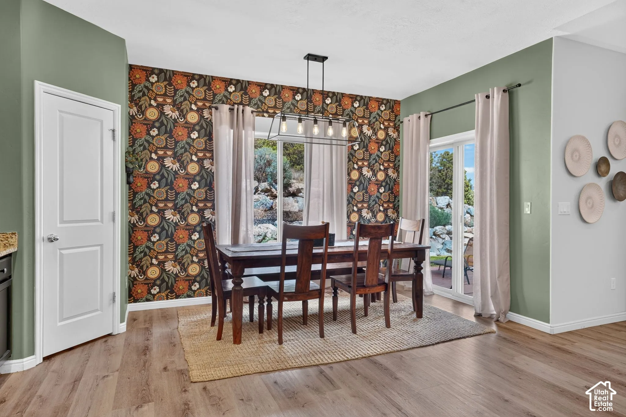 Wood-finish flooring, accent wall with patterned wallpaper, pendant lighting fixture, and sliding glass doors