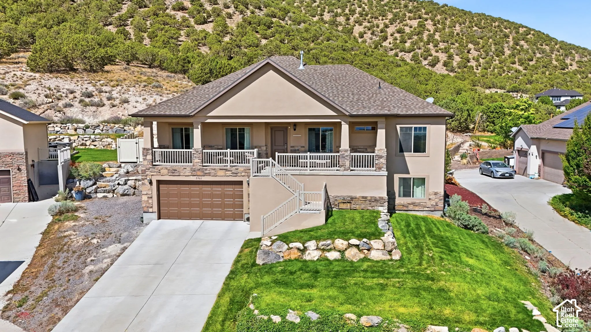 Stucco and stone exterior with a covered balcony, integrated garage, concrete driveway, and tiered landscaping