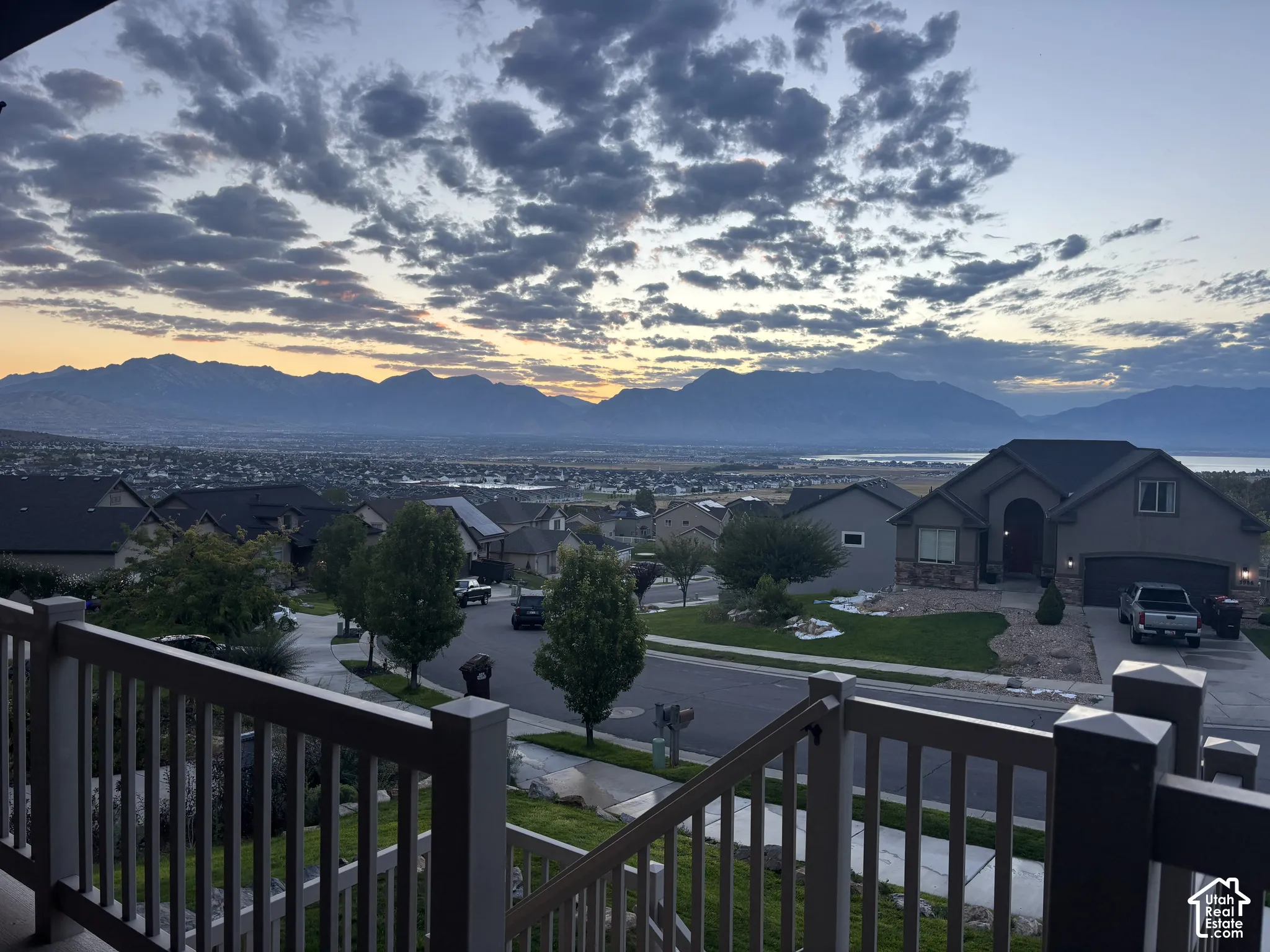 View from the front porch.  Expansive mountain backdrop, distant body of water, and surrounding neighborhood from a property featuring a railing with balusters