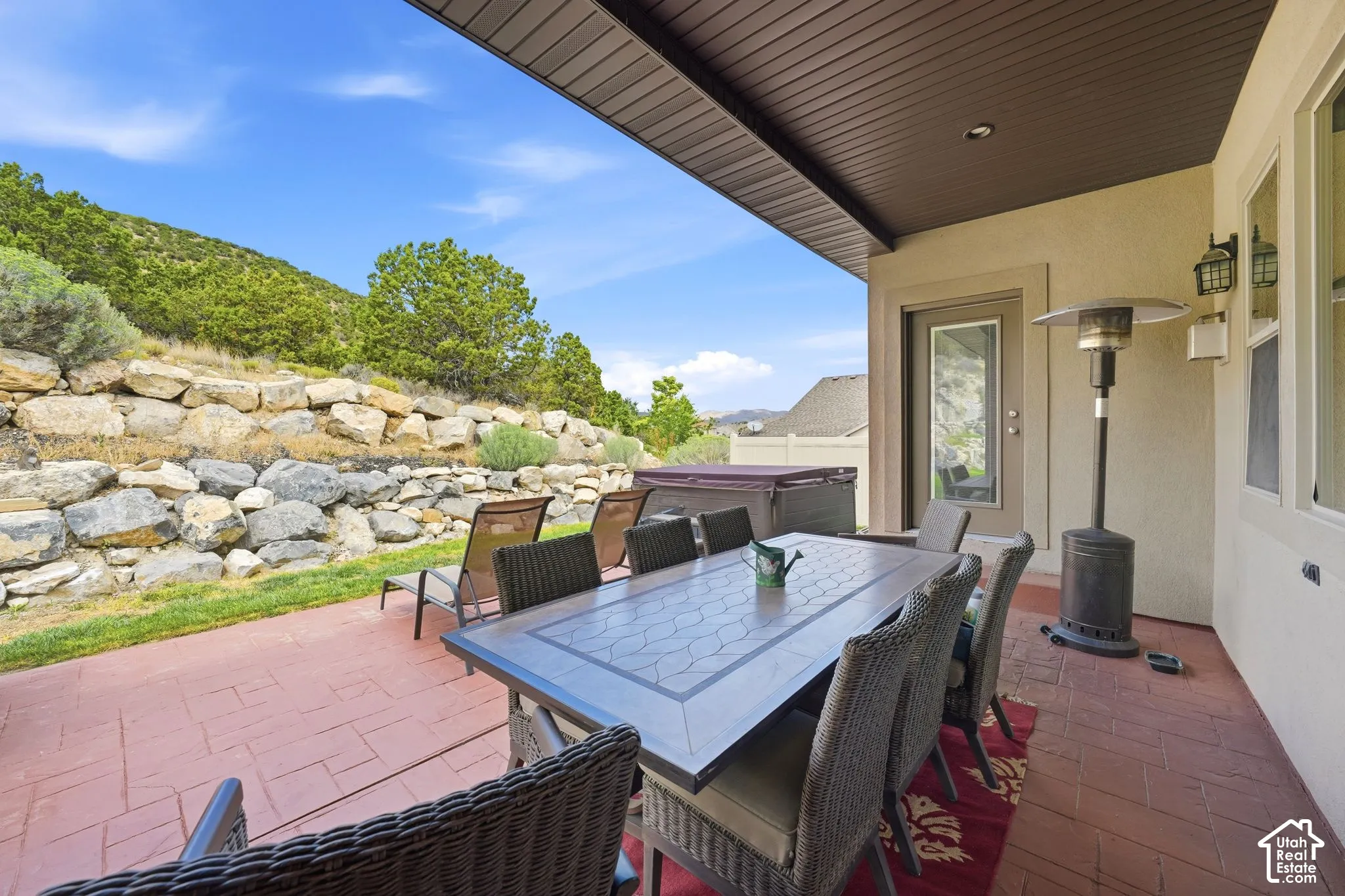 Covered patio featuring stamped concrete flooring, exterior sconce lighting, and a retaining wall with natural stone