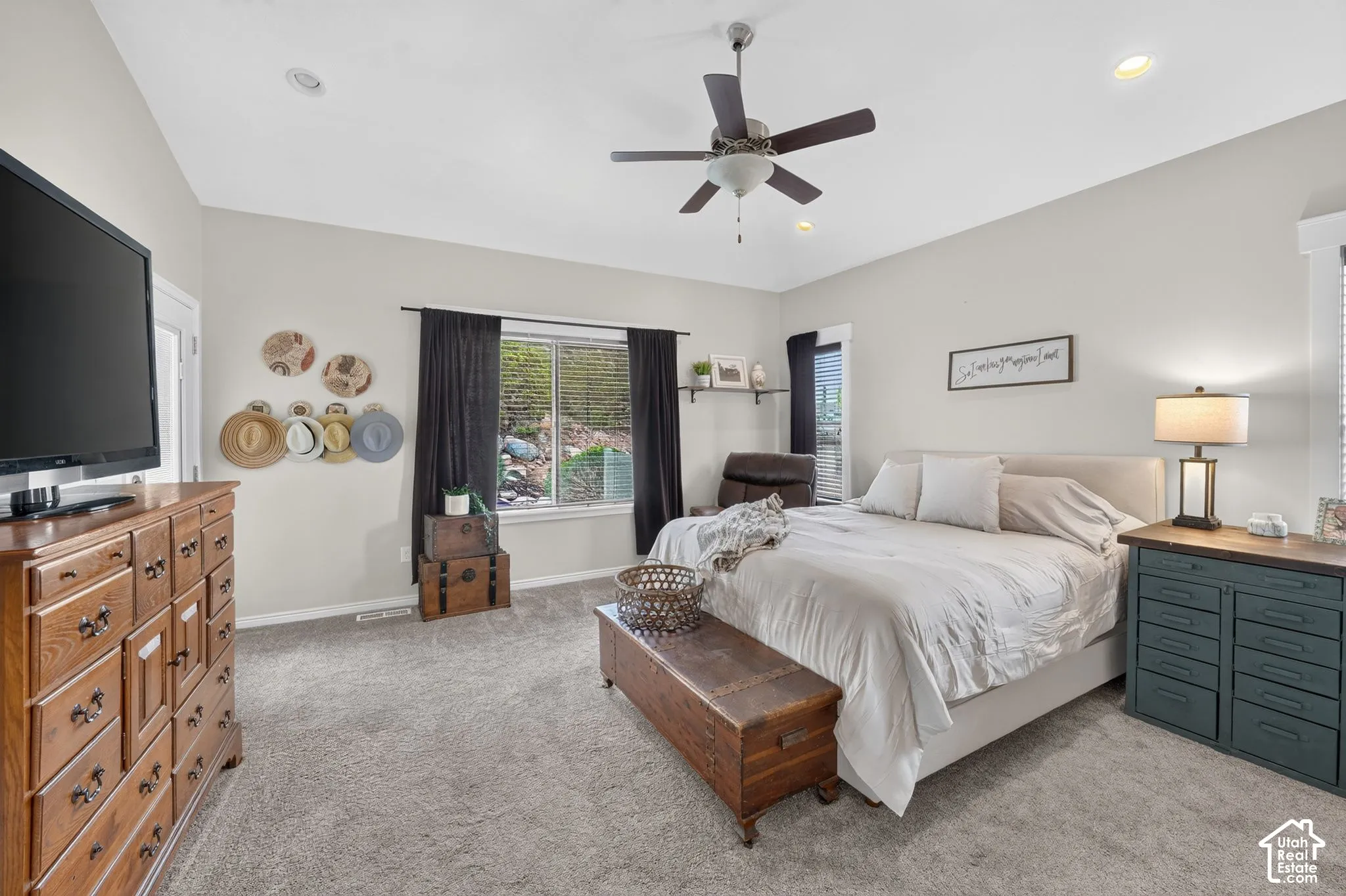Recessed lighting, ceiling fan, broad window with dark-toned drapes, light-colored carpeting, and a neutral wall palette
