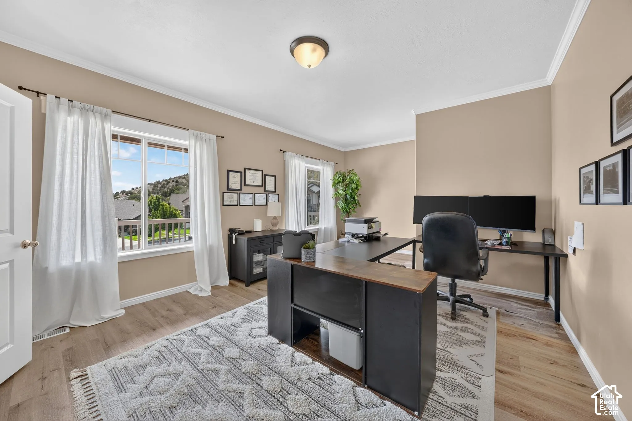 Spacious room with wood-finish flooring, two large windows, neutral wall paint, and crown molding