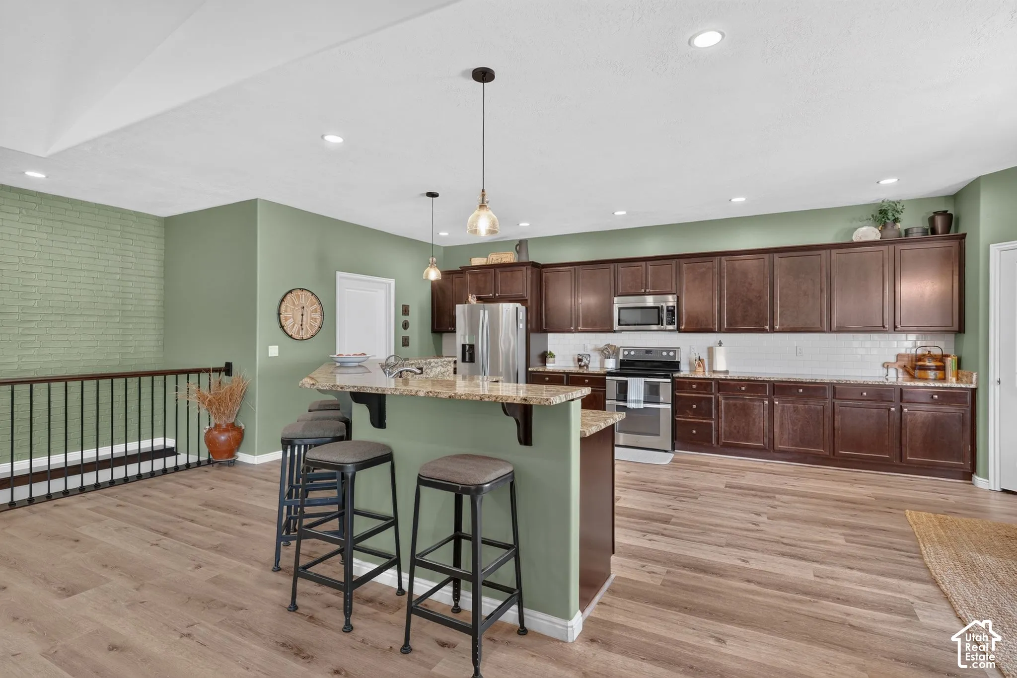 Kitchen with dark wood cabinetry, stainless steel appliances, a white subway tile backsplash, and a breakfast bar with stone-finish countertop
