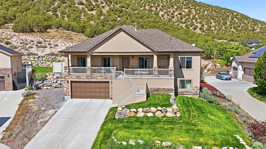 Stucco and stone exterior with a covered balcony, integrated garage, concrete driveway, and tiered landscaping