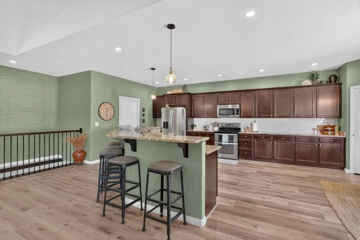 Kitchen with dark wood cabinetry, stainless steel appliances, a white subway tile backsplash, and a breakfast bar with stone-finish countertop